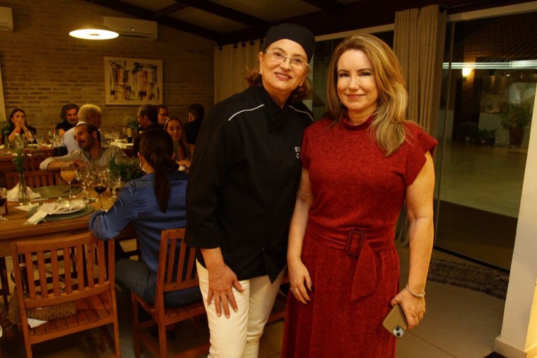 Sylvia Cury, de dólmã preto, com a convidada de vestido vermelho, no salão